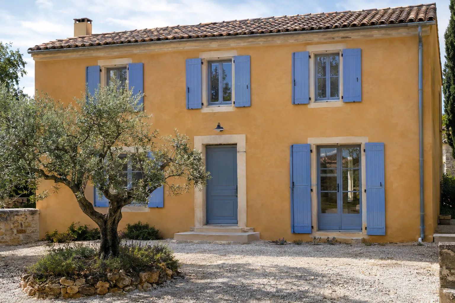 Façade de bastide ocre rénovée, enduit à la chaux terminé, volets bleu lavande neufs et olivier devant la porte.